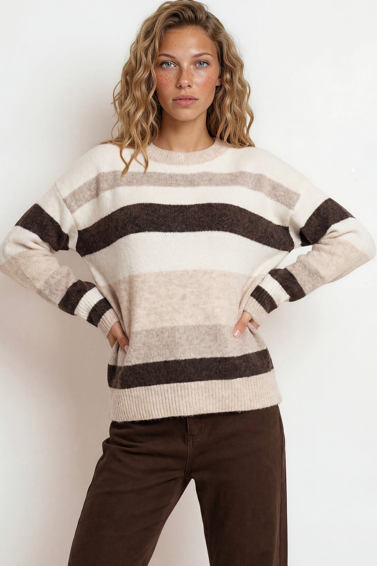 Woman wearing a striped sweater and brown pants against a white background