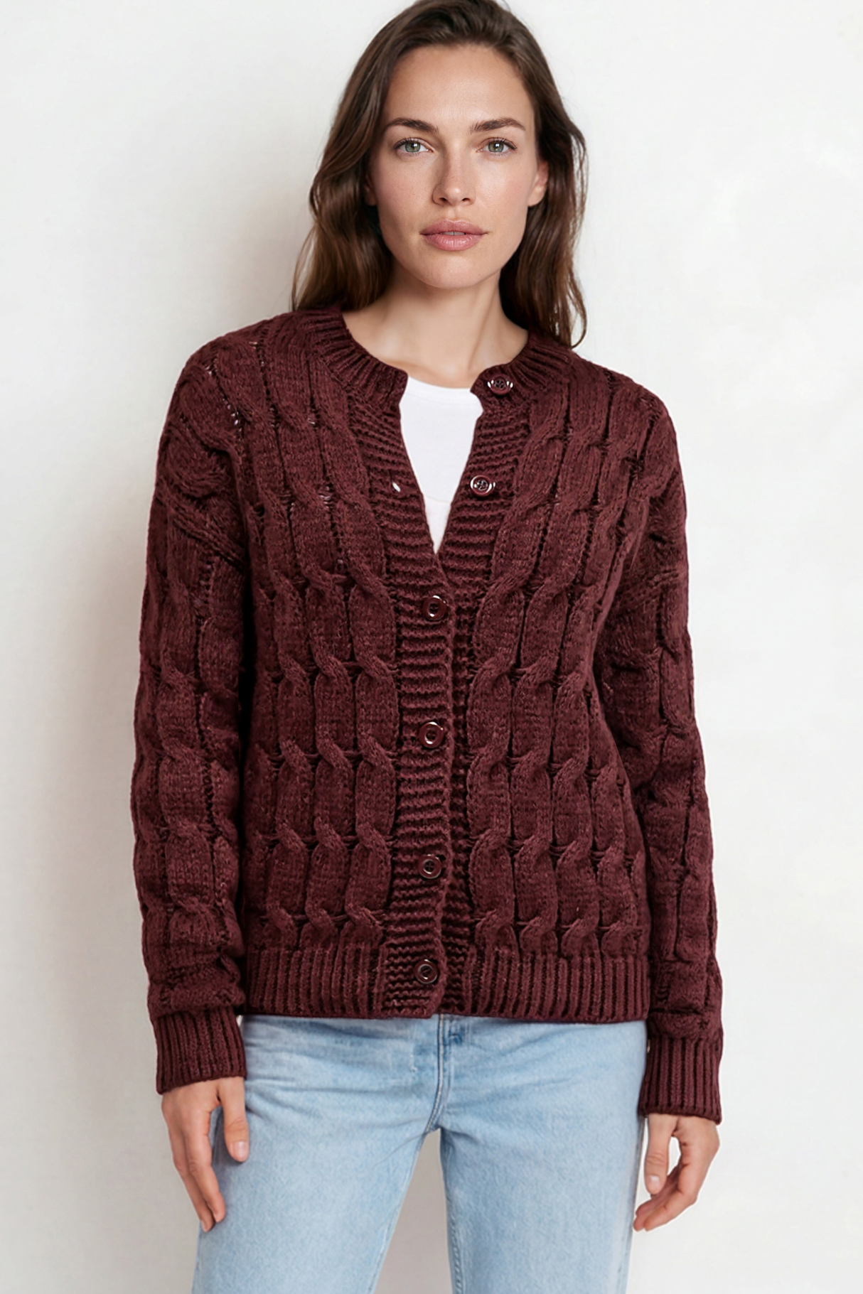 Woman wearing a brown cable knit sweater and light blue jeans on a white background