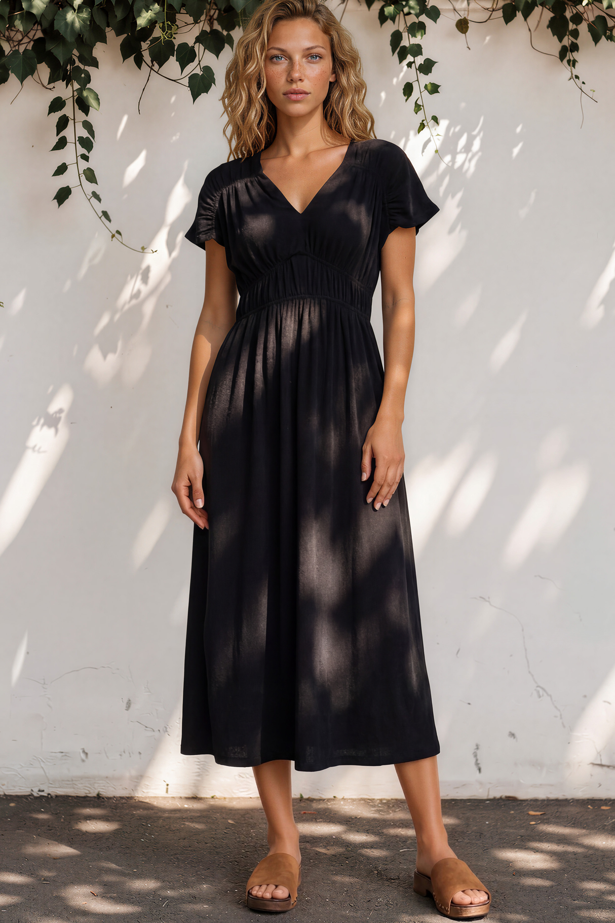Woman wearing a black dress standing against a white wall with greenery.
