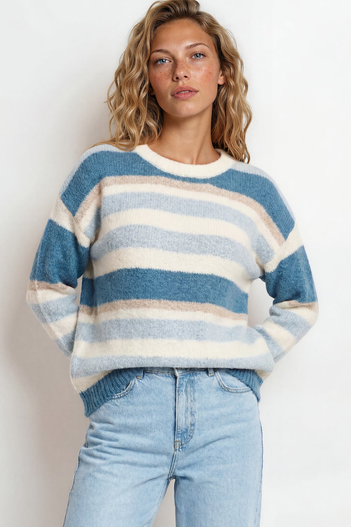 Woman wearing a blue and white striped sweater with light blue jeans against a plain background