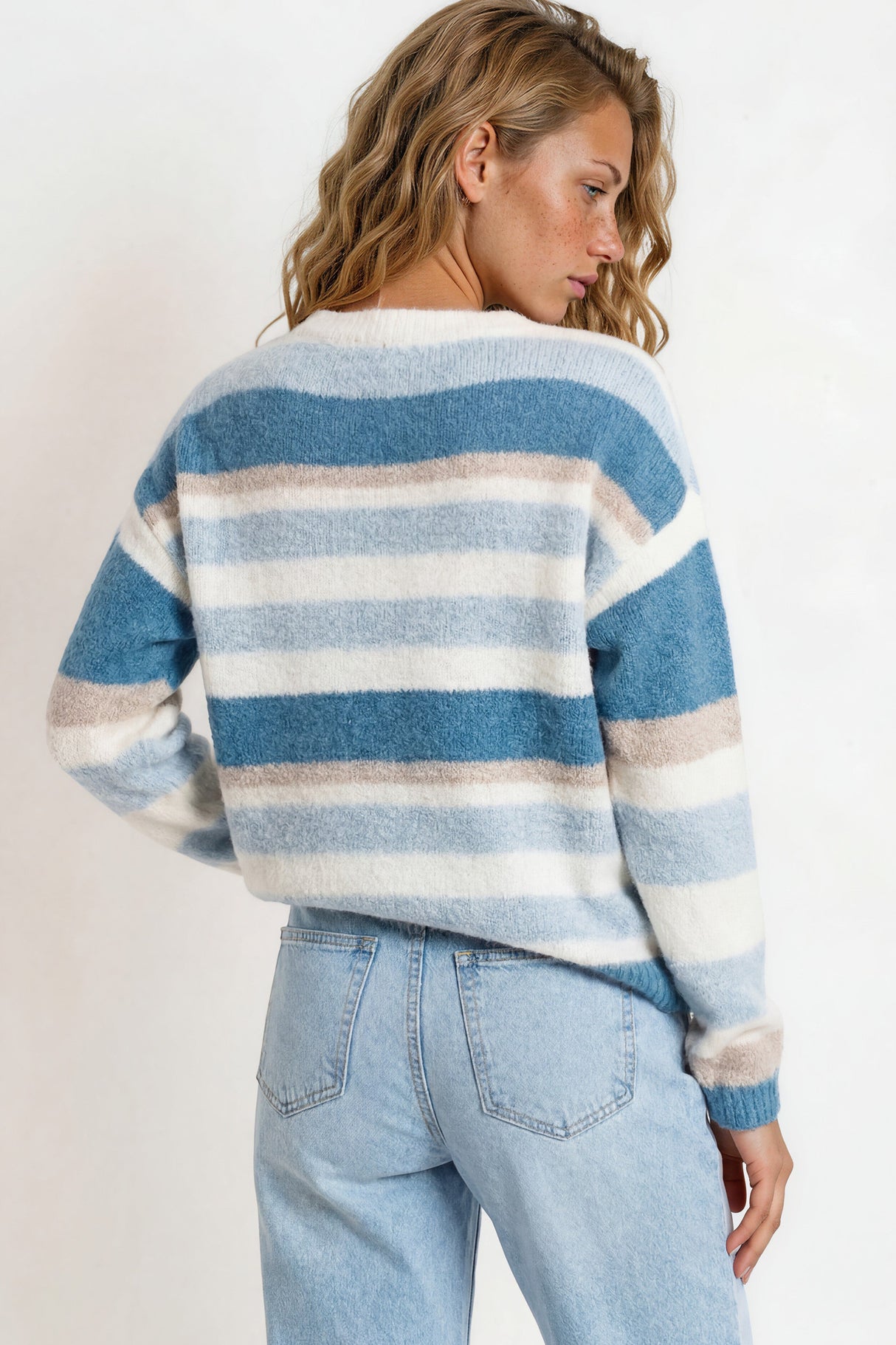 Woman wearing a blue and white striped sweater and light blue jeans on a plain background