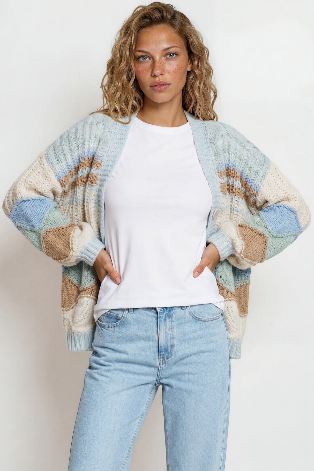 Woman wearing a patterned cardigan over a white shirt and jeans on a plain background