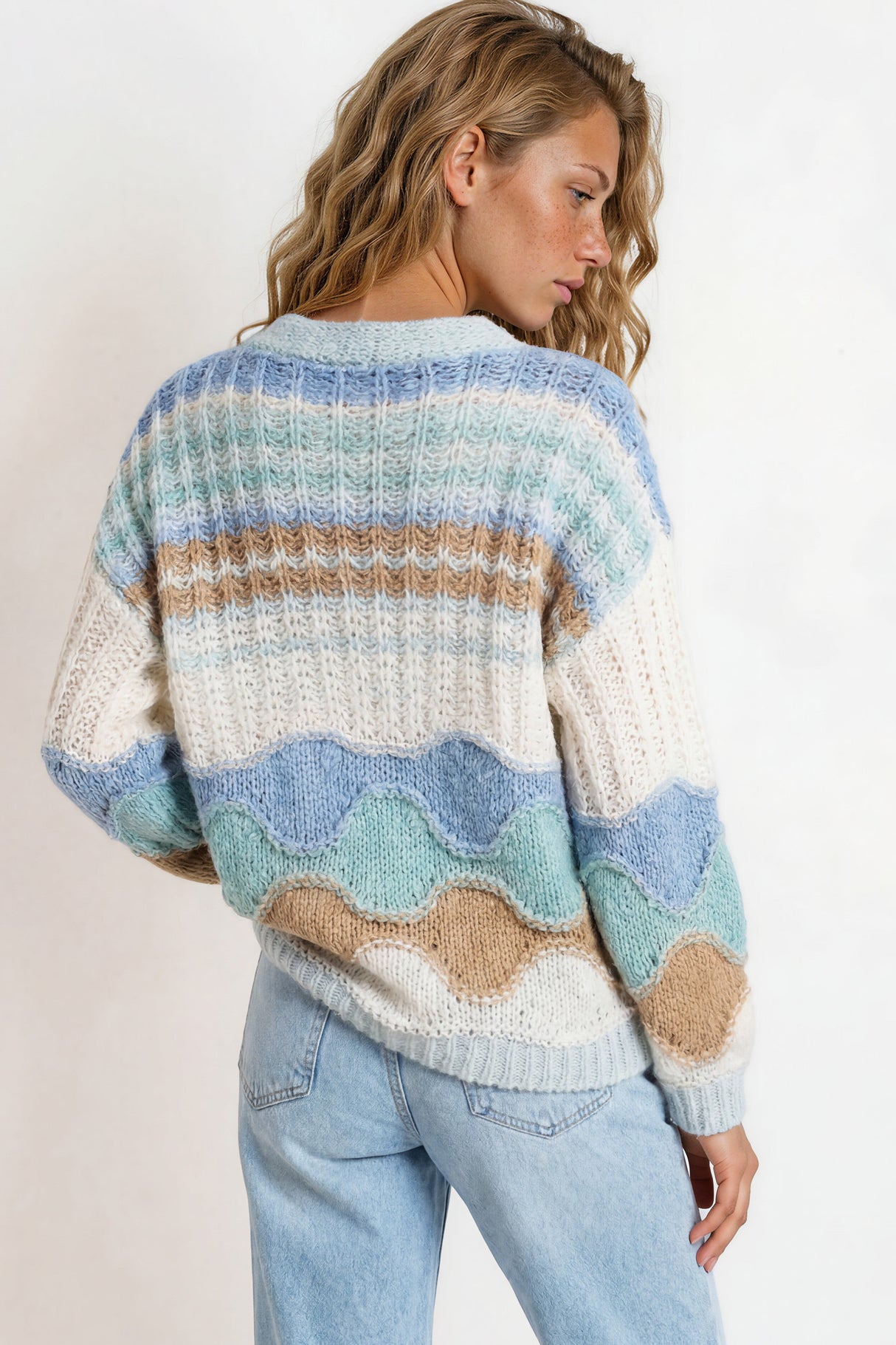 Woman wearing a colorful striped sweater and jeans on a plain background