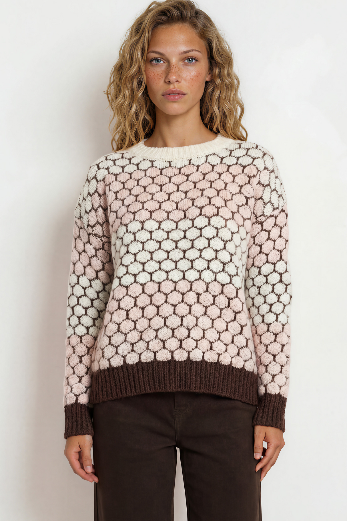Woman wearing a patterned sweater and dark pants against a white background