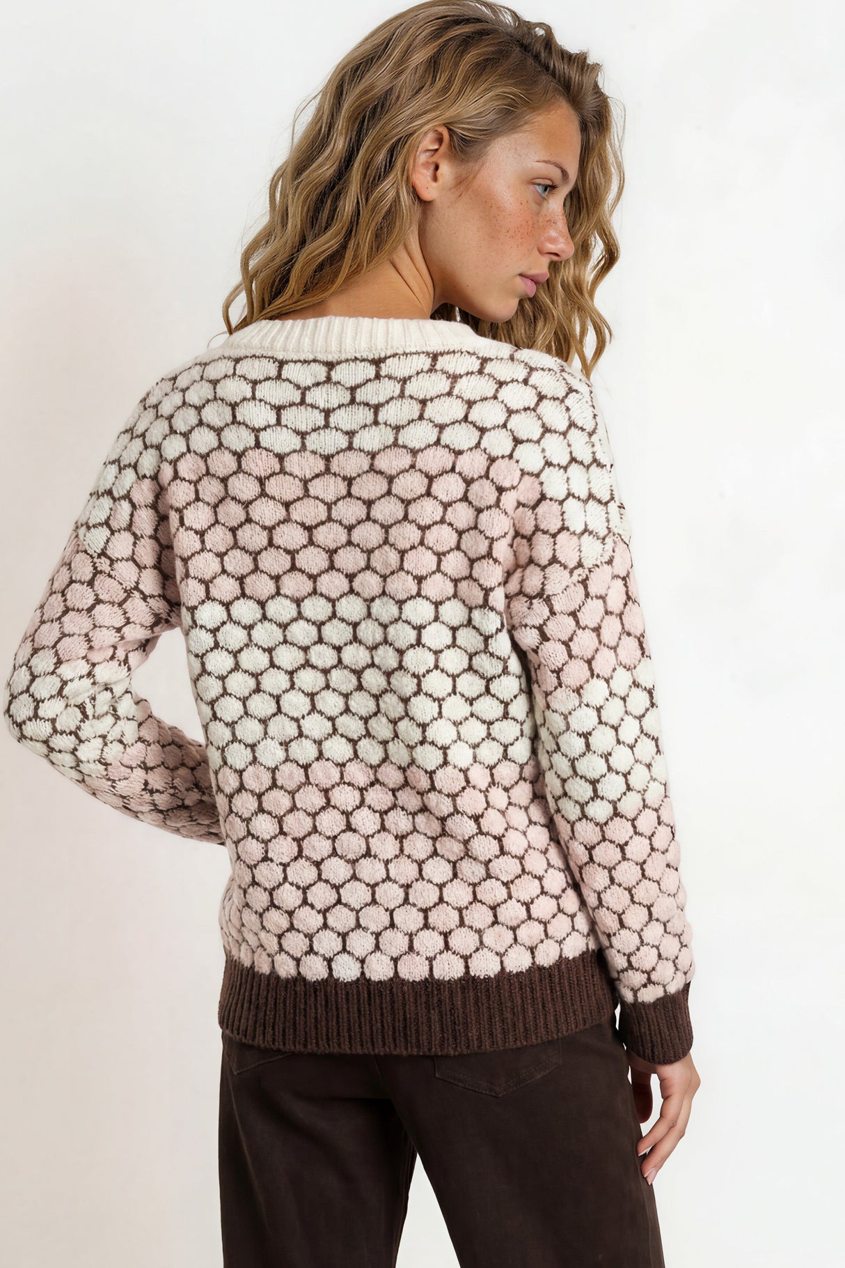 Woman wearing a patterned sweater and dark pants against a plain background