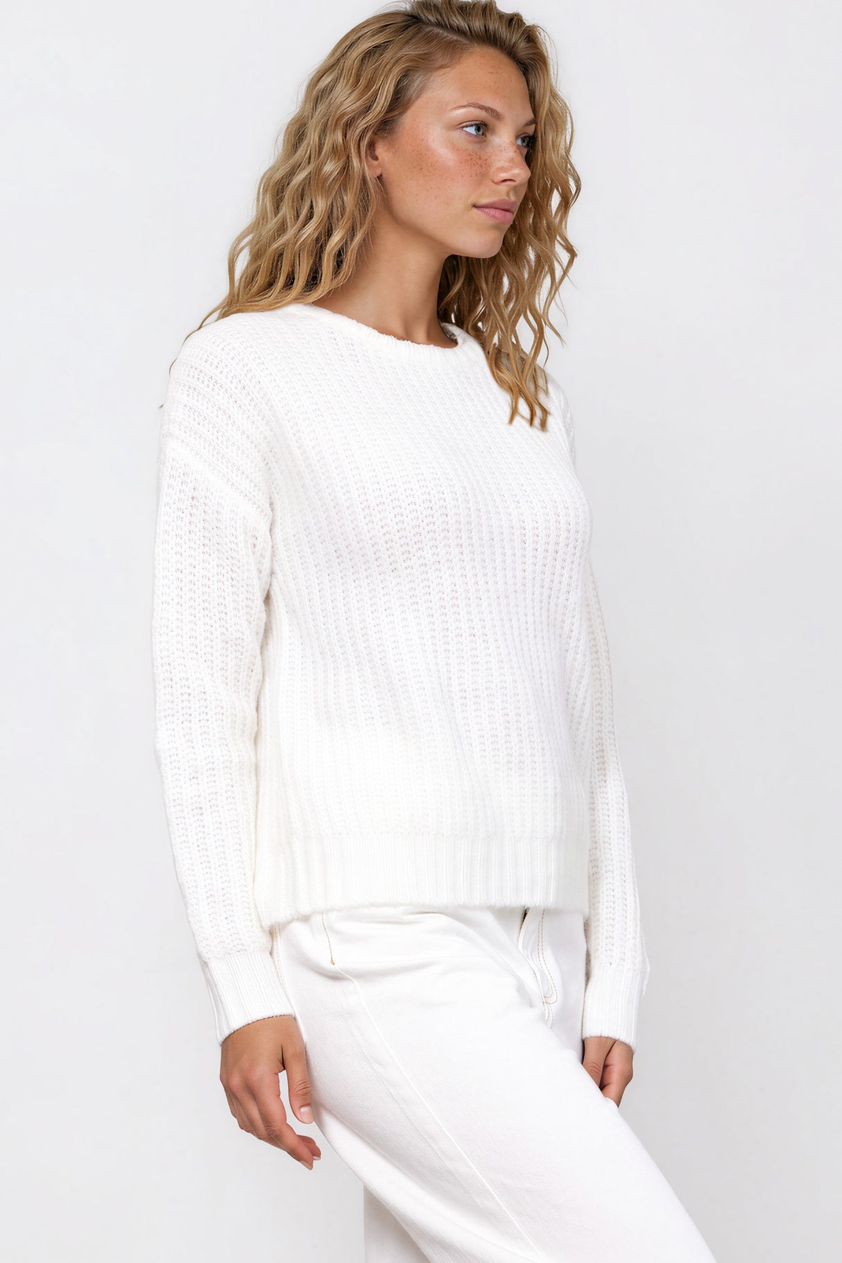 Woman wearing a white sweater and pants against a neutral background