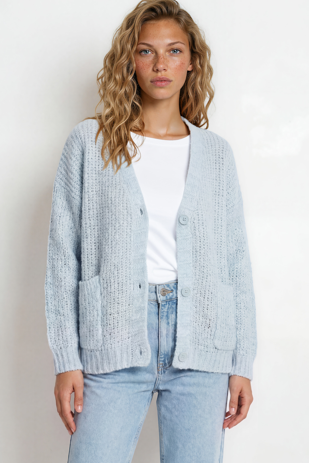 Woman wearing a light blue cardigan over a white shirt and jeans on a plain background