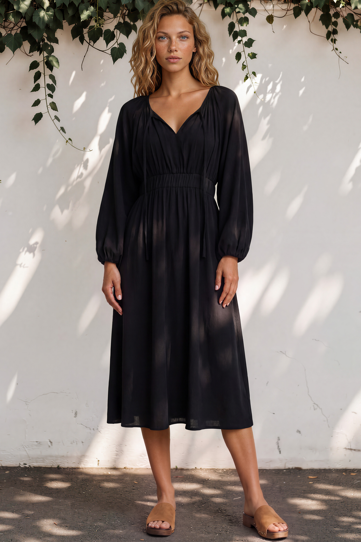 Woman wearing a black dress standing against a white wall with greenery.