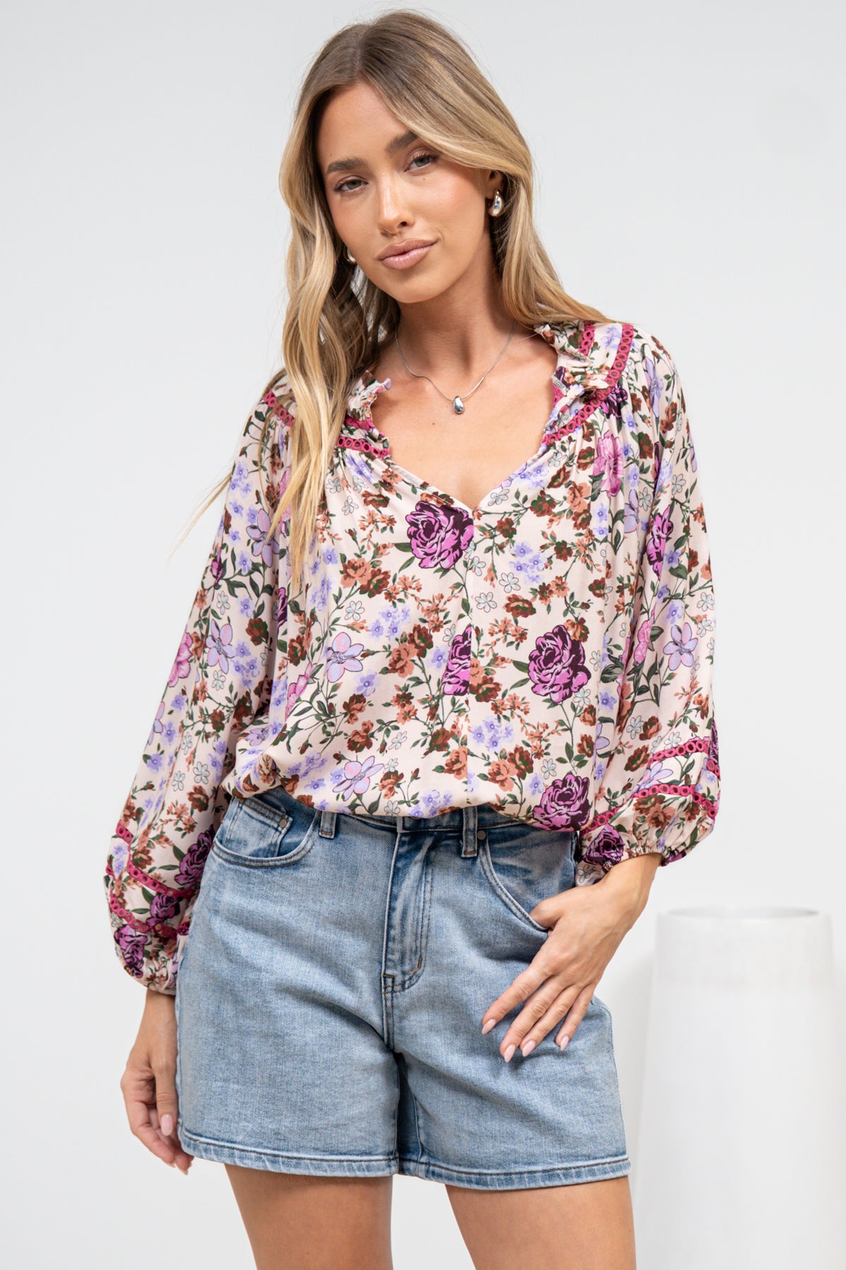 A woman in a flowing beige blouse featuring an all-over print and relaxed silhouette, posed against an off-white painted wall.