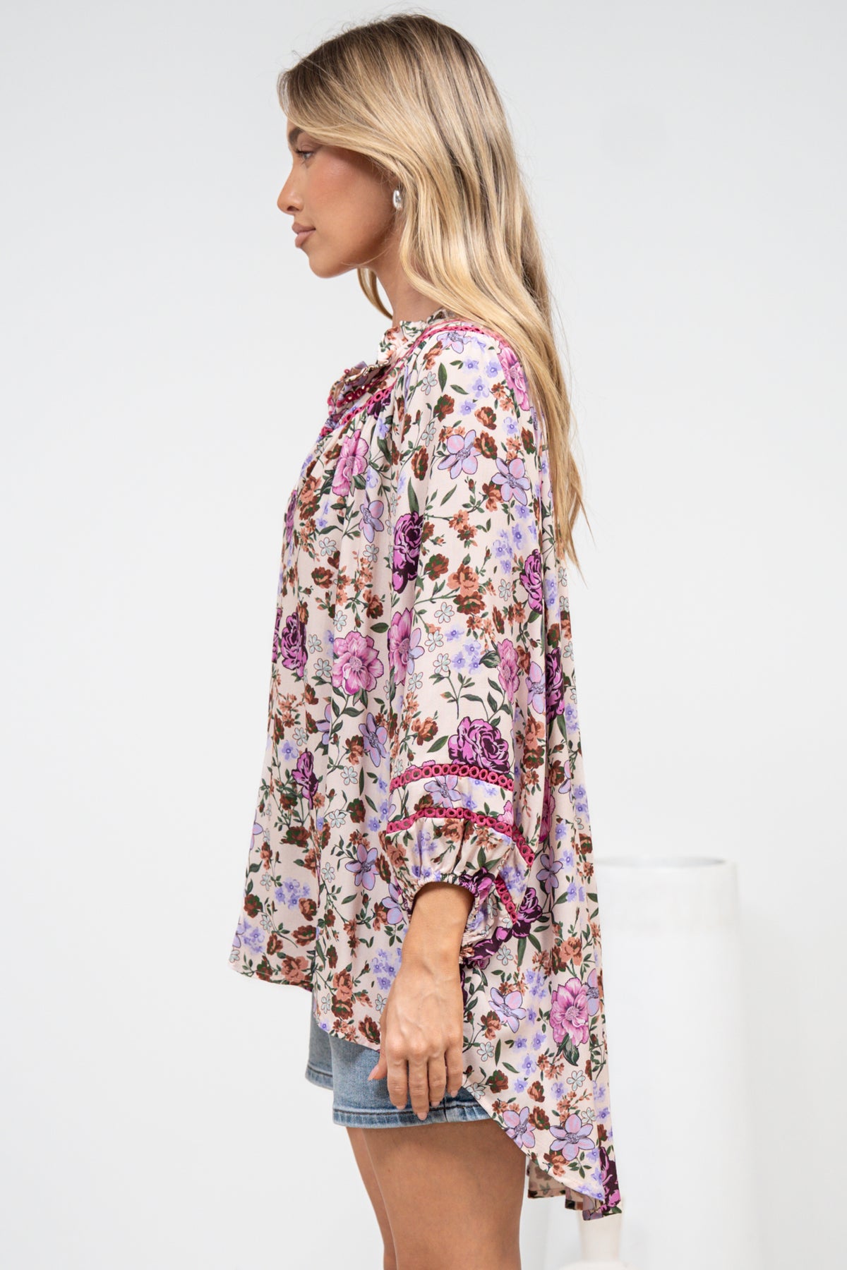 A woman in a flowing beige blouse featuring an all-over print and relaxed silhouette, posed against an off-white painted wall.