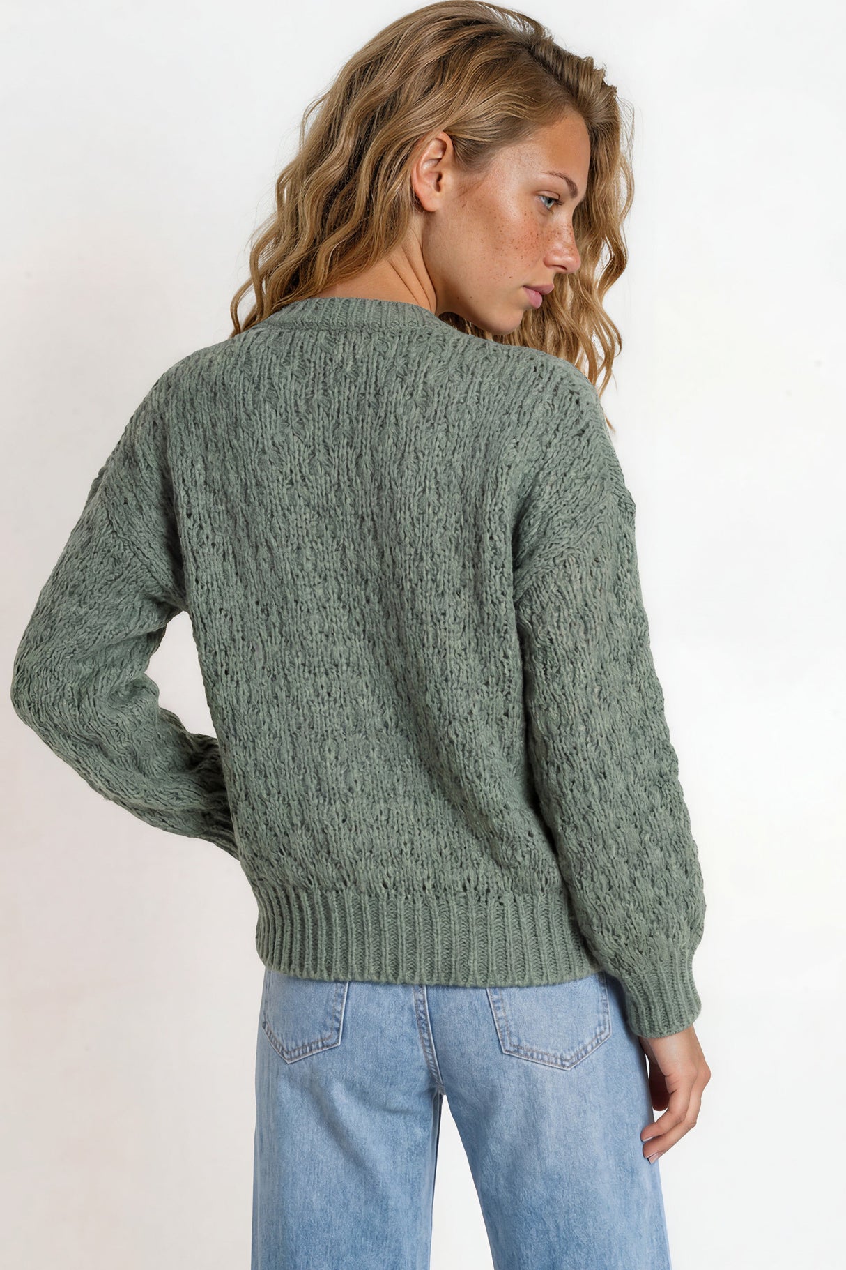Woman wearing a green sweater and blue jeans against a white background