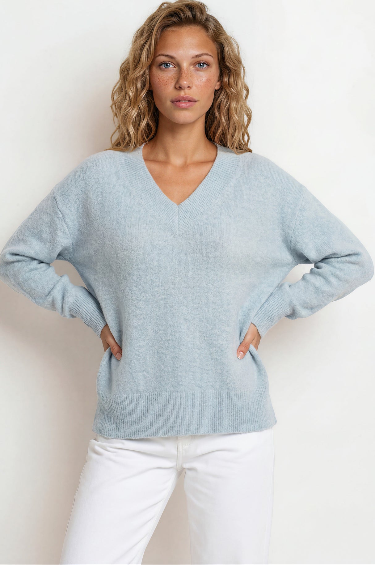 Woman wearing a light blue sweater and white pants against a plain background