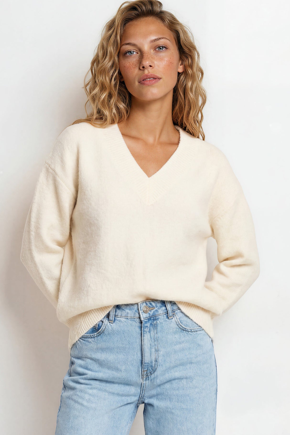 Woman wearing a cream sweater and light blue jeans against a white background