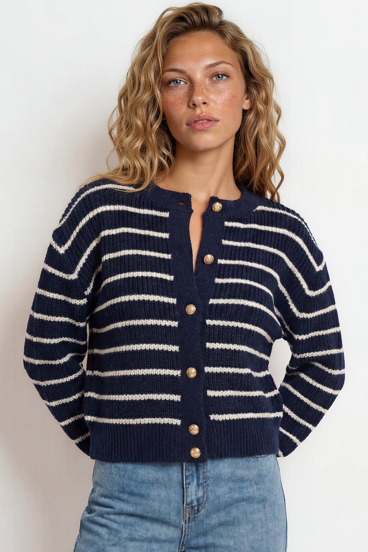 Woman wearing a navy and white striped sweater with blue jeans against a plain background