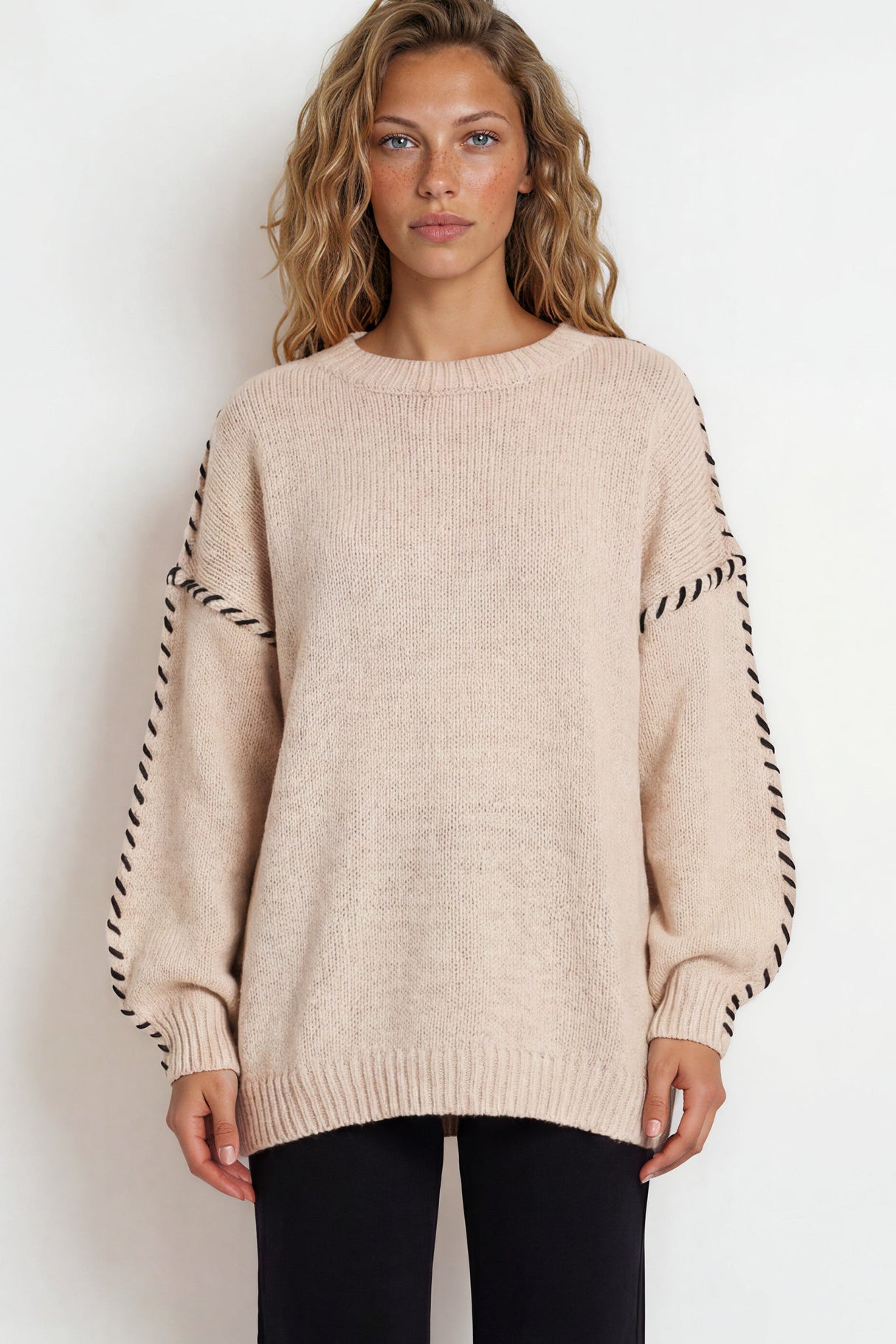 Woman wearing a beige sweater with black and white striped sleeves on a white background