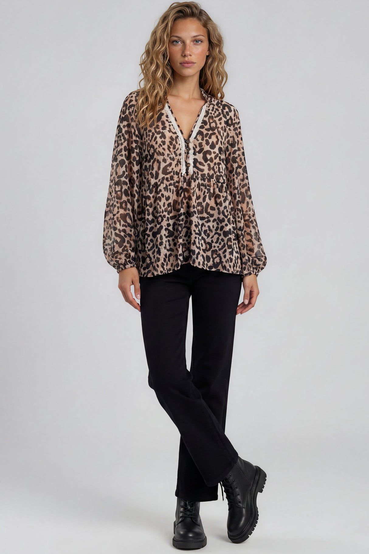 Woman wearing a leopard print blouse with black pants and boots on a white background