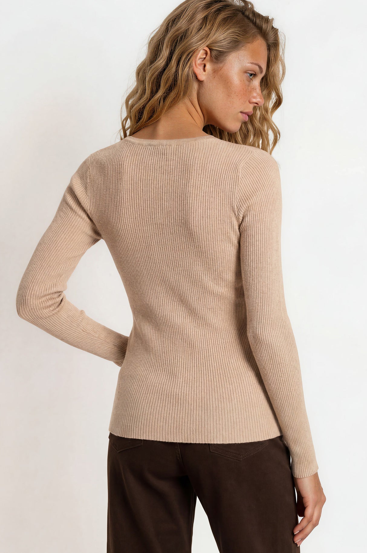 Woman wearing a beige sweater and brown pants on a white background