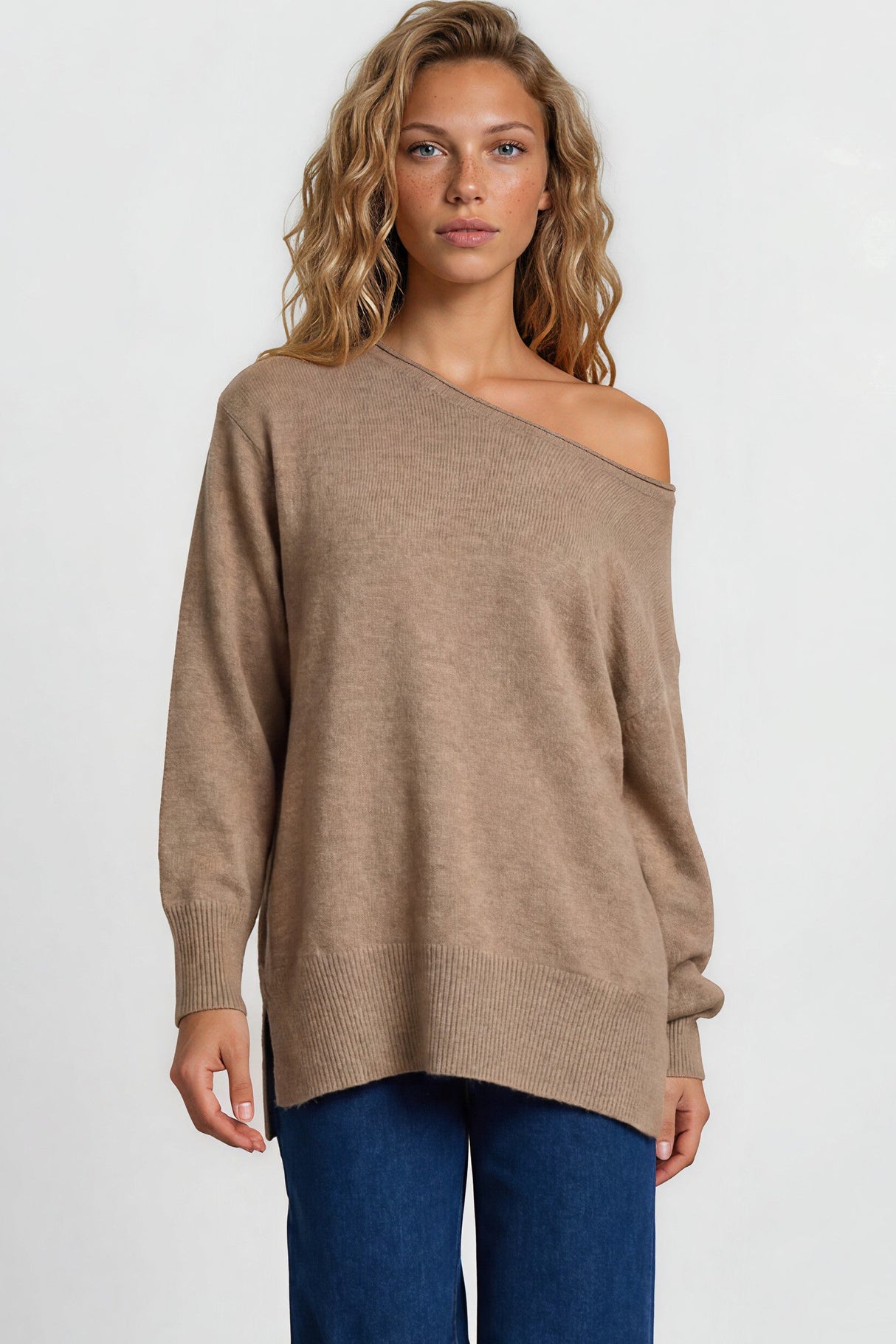 Woman wearing a beige off-shoulder sweater and blue jeans on a white background