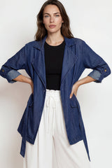 Woman wearing a blue jacket, black top, and white pants on a white background