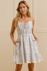 A woman modeling a light blue and white striped tiered cotton dress with pockets, standing in a bright room with cream-colored cabinets and a large mirror showing her reflection.