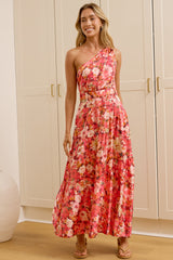 A woman stands in a bright room wearing a one-shoulder floral maxi dress with a red, pink, and white pattern. She is positioned in front of white built-in wardrobes, with a large floor-to-ceiling mirror on the left reflecting her side profile.