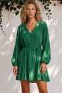 Woman wearing a green dress standing against a white wall with greenery.