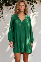 Woman wearing a green dress standing against a white wall with greenery.