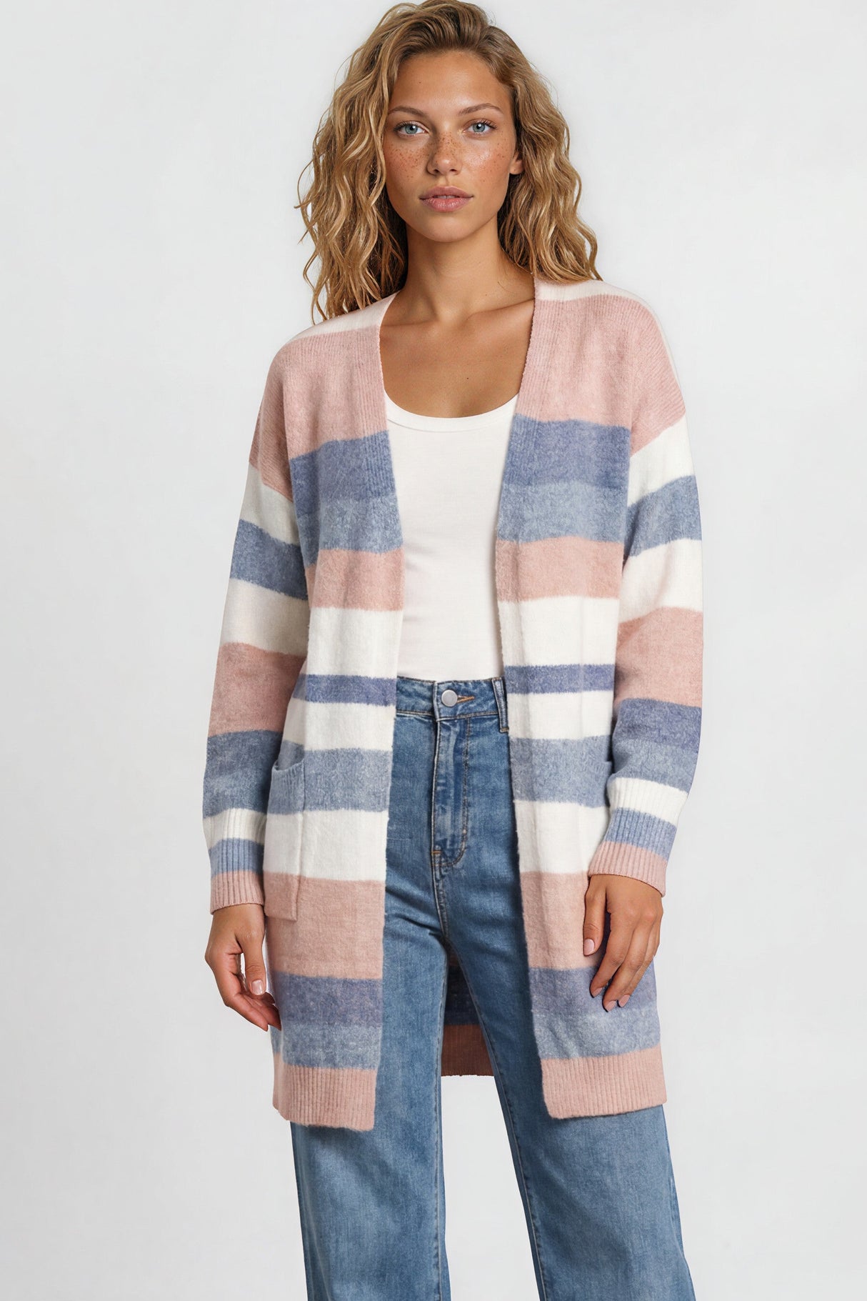 Woman wearing a striped cardigan, white top, and blue jeans against a plain background