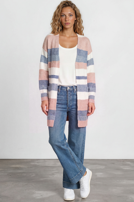 Woman wearing a striped cardigan, white top, blue jeans, and white sneakers on a plain background