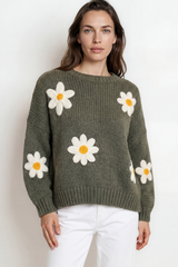 Woman wearing a green sweater with white daisy flowers on a plain background