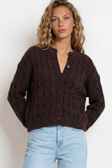 Woman wearing a brown cable knit cardigan and light blue jeans on a white background