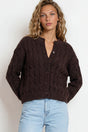Woman wearing a brown cable knit cardigan and light blue jeans on a white background
