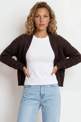 Woman wearing a brown cardigan, white shirt, and light blue jeans against a white background