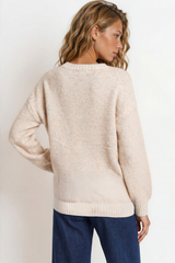 Woman wearing a beige sweater and blue pants against a white background