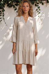 Woman wearing a beige dress standing against a white wall with greenery.