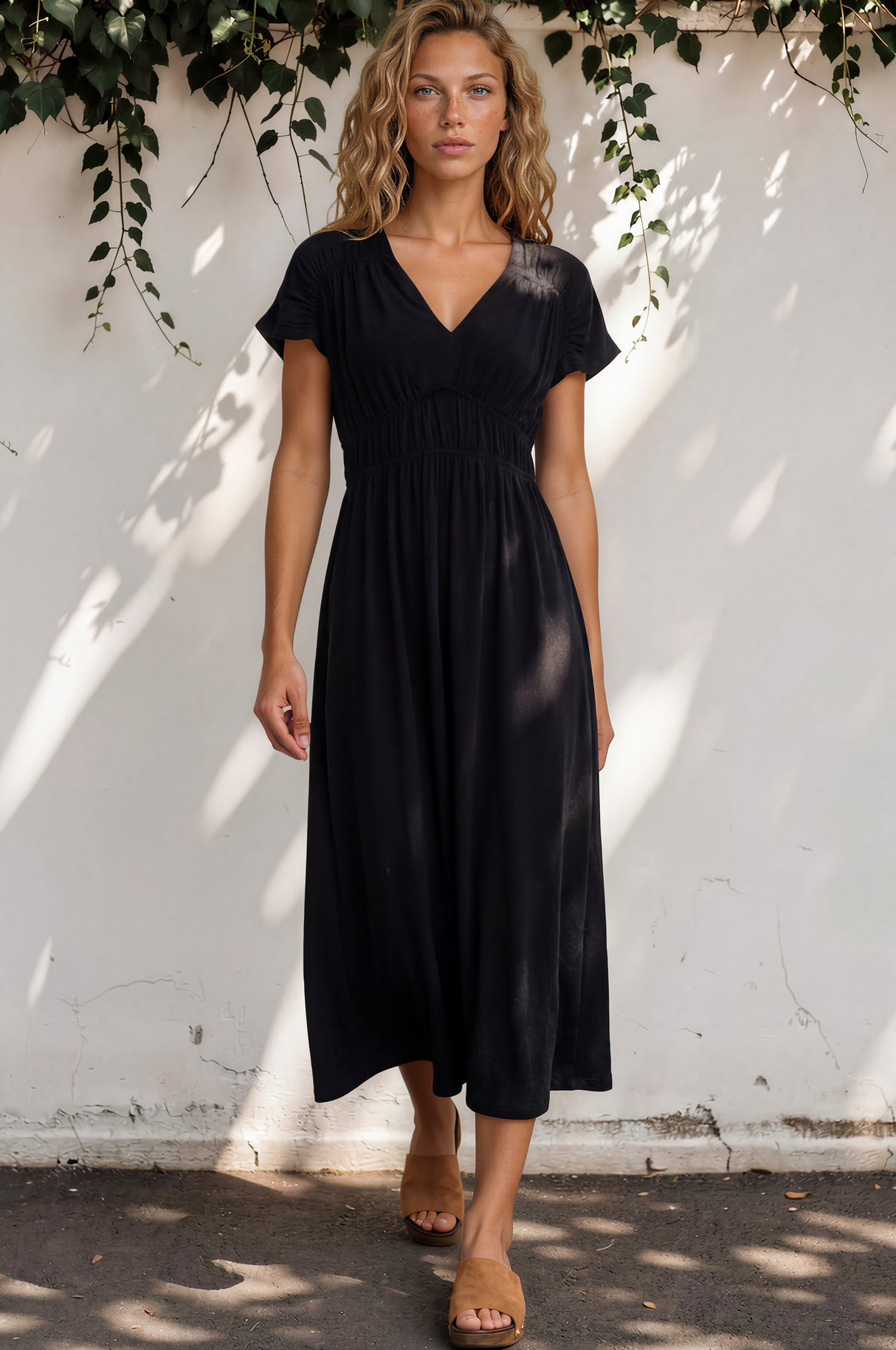 Woman wearing a black dress standing against a white wall with greenery.