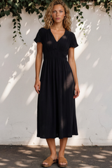 Woman wearing a black dress standing against a white wall with greenery.