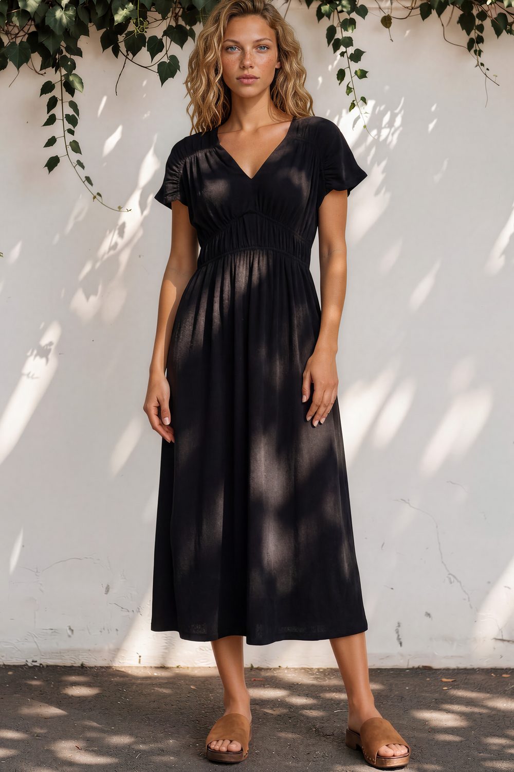 Woman wearing a black dress standing against a white wall with greenery.