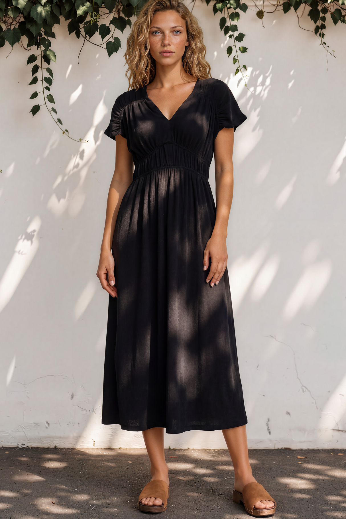 Woman wearing a black dress standing against a white wall with greenery.