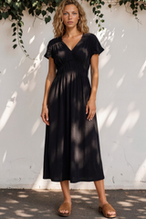 Woman wearing a black dress standing against a white wall with greenery.