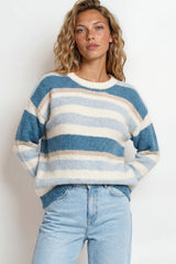 Woman wearing a blue and white striped sweater with light blue jeans against a plain background