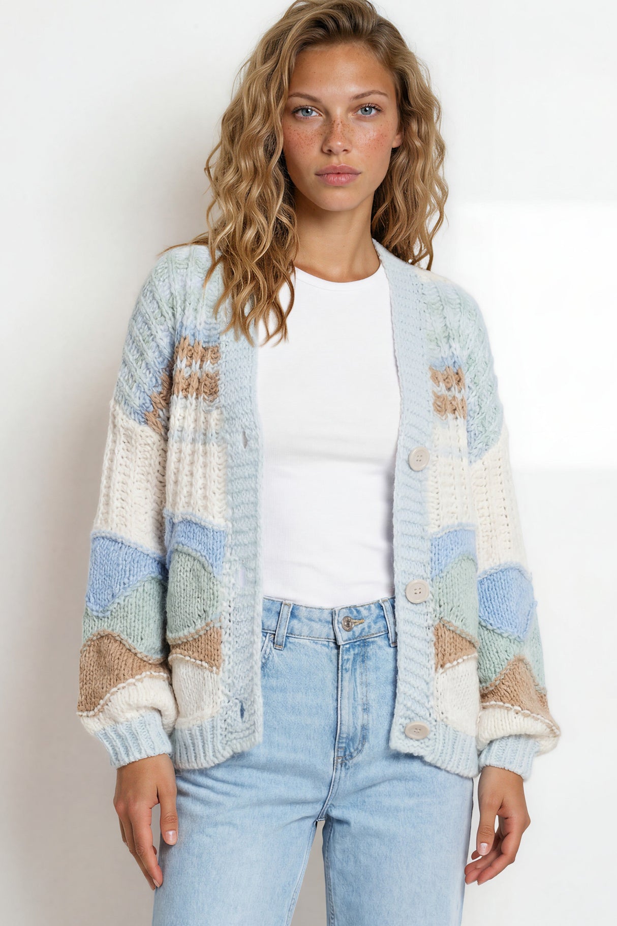 Woman wearing a patterned cardigan and jeans against a plain background