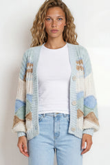 Woman wearing a patterned cardigan, white shirt, and light blue jeans on a plain background