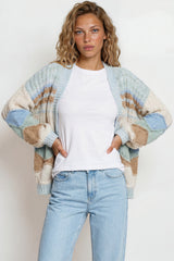 Woman wearing a patterned cardigan over a white shirt and jeans on a plain background