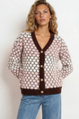Woman wearing a patterned cardigan with brown trim against a white background