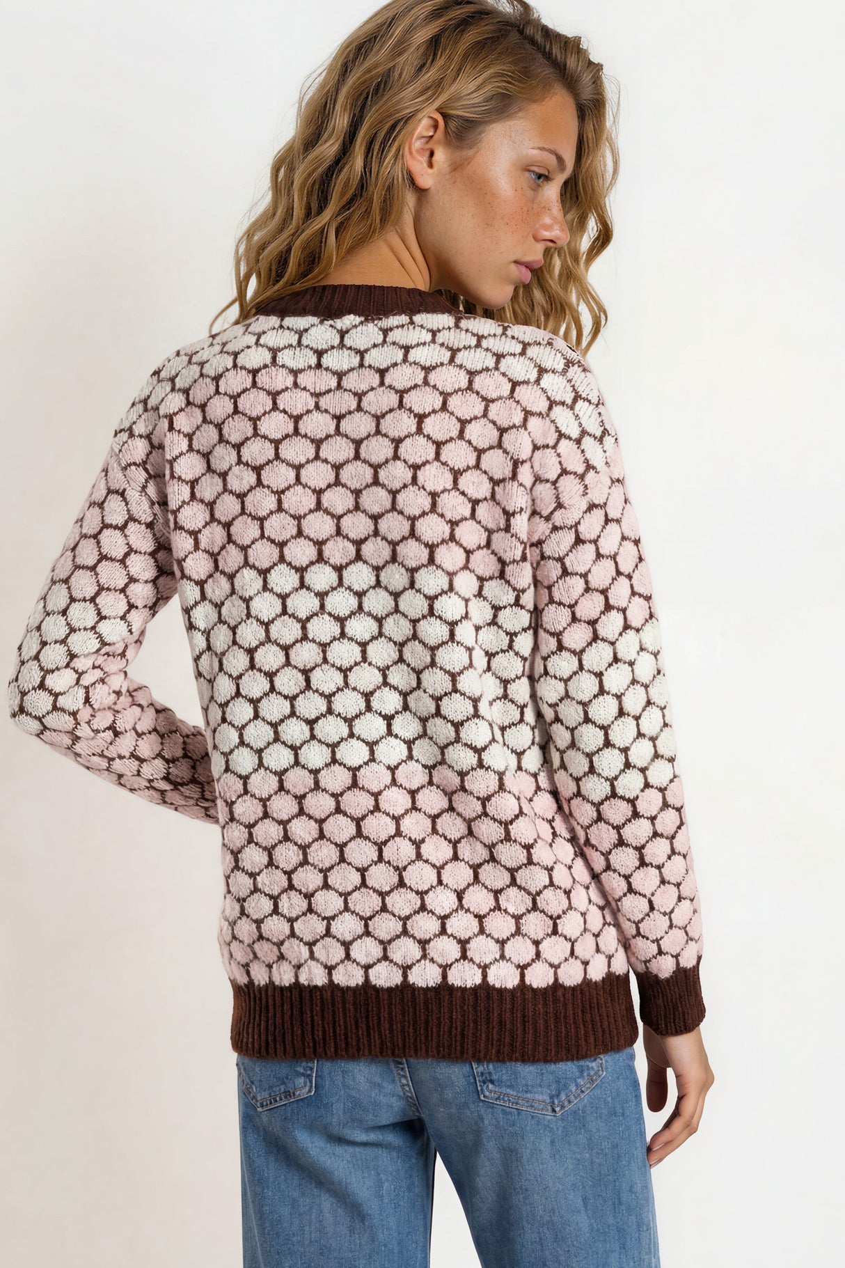 Woman wearing a patterned sweater and jeans on a plain background