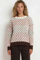 Woman wearing a patterned sweater and dark pants against a white background
