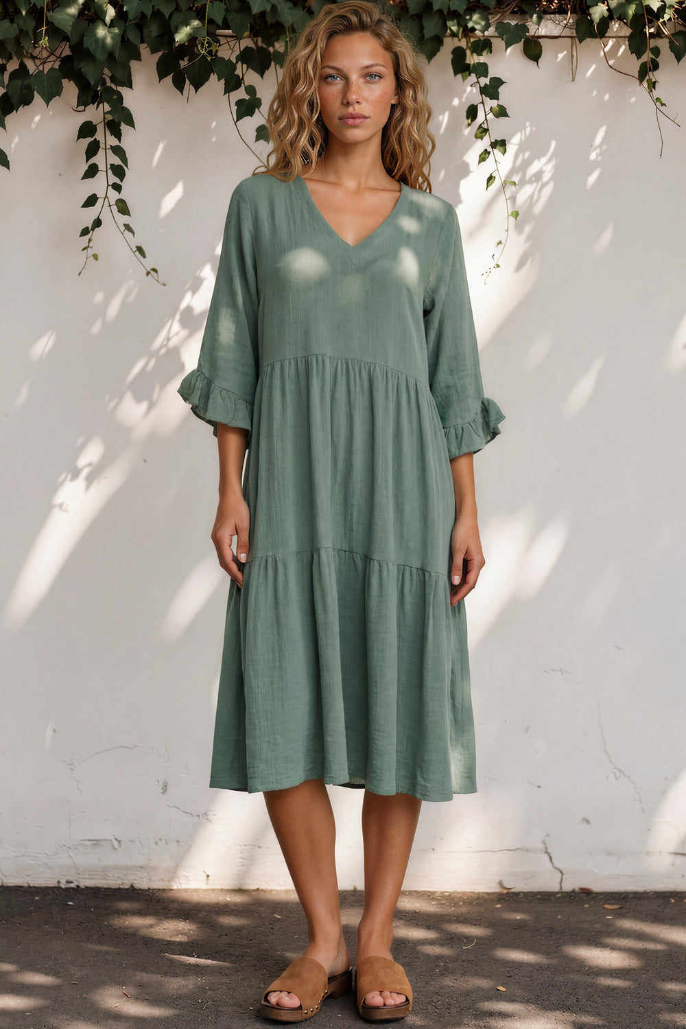 Woman wearing a green dress standing against a white wall with greenery.