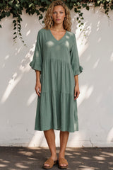 Woman wearing a green dress standing against a white wall with greenery.