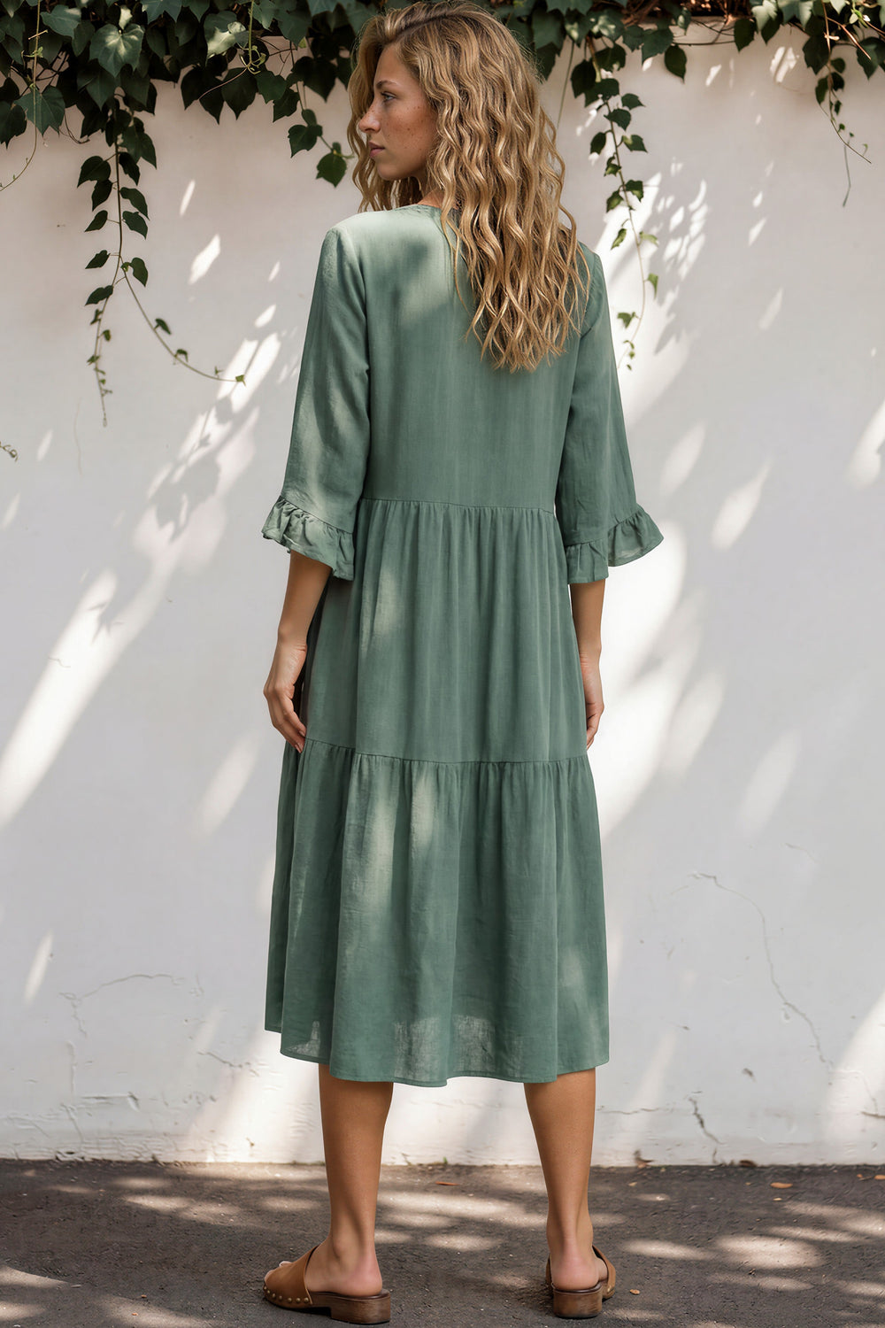 Woman wearing a green dress standing against a white wall with greenery.